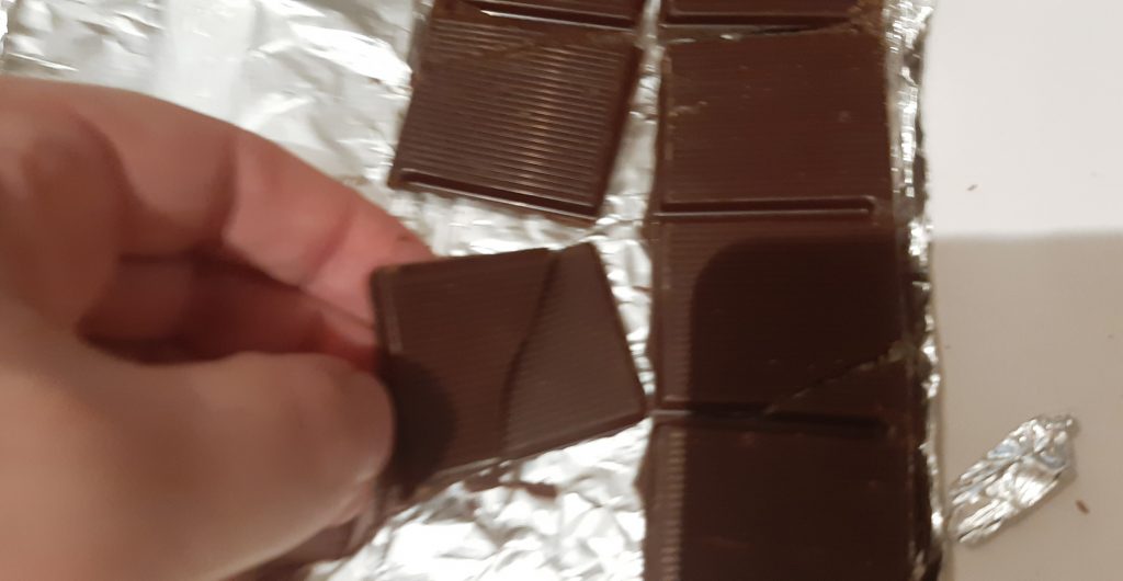 Covek drzi kockicu cokolade u ruci